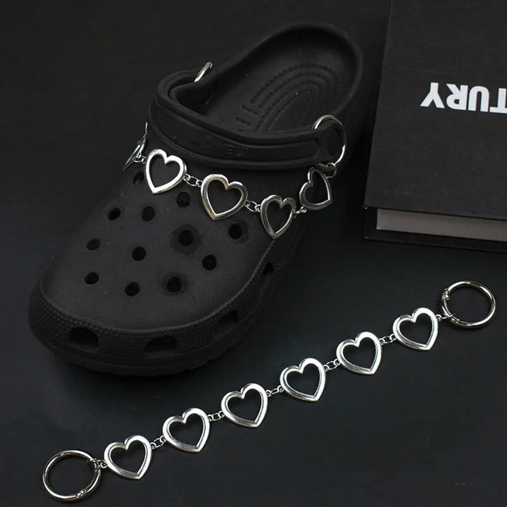 Black clog shoe with a silver heart-shaped charm on a dark background