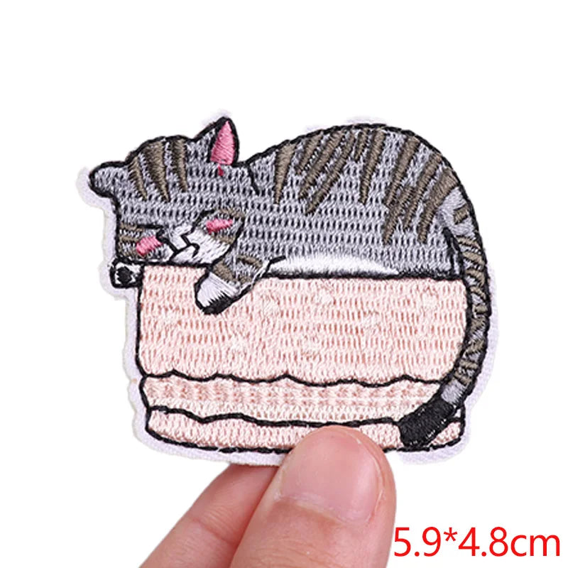 Embroidered patch of a cat sleeping on a cushion held by a hand with dimensions displayed.