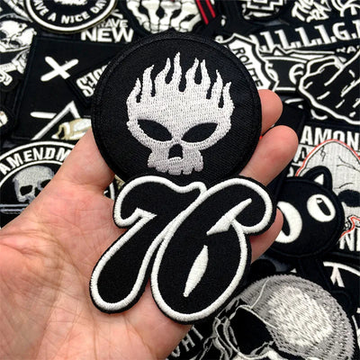 Black and white patch with skull design held in a hand, surrounded by other patches.