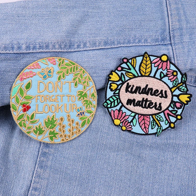 Two embroidered patches on a denim jacket, one with 'Don't forget to look up' and the other with 'Kindness matters'.