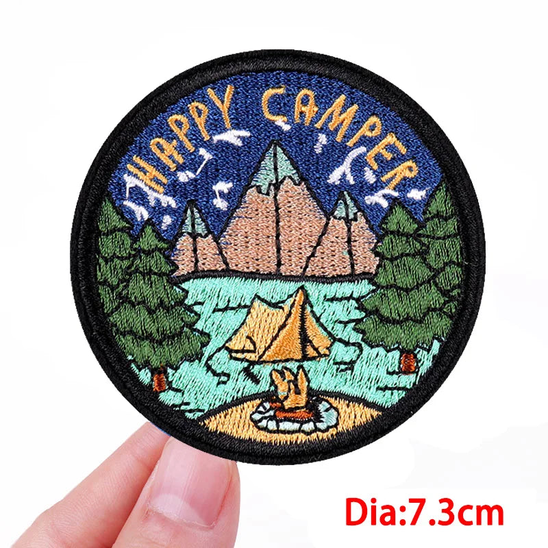 Circular patch with 'Happy Camper' design held by a hand, on a white background.