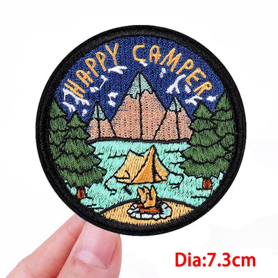 Circular patch with 'Happy Camper' design held by a hand, on a white background.