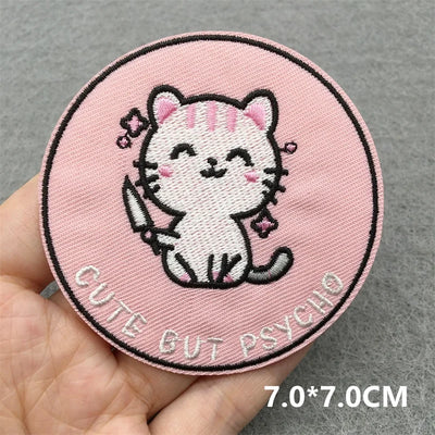 Circular patch with a cartoon cat and text 'Cute But Psycho' held in hand on a gray background