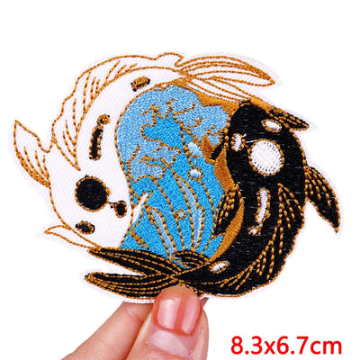 Embroidered patch of two fish on a white background with a hand holding it.