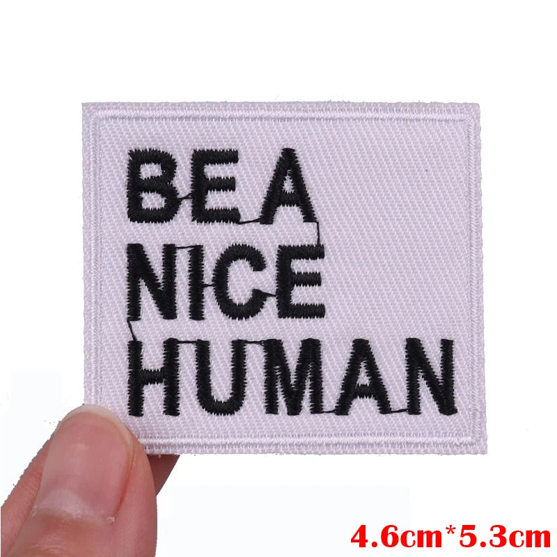 Patch with 'BE A NICE HUMAN' text held by a hand on a white background
