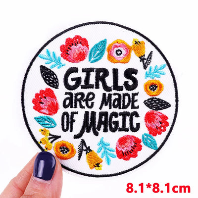 Circular patch with floral design and 'GIRLS ARE MADE OF MAGIC' text held by a hand.