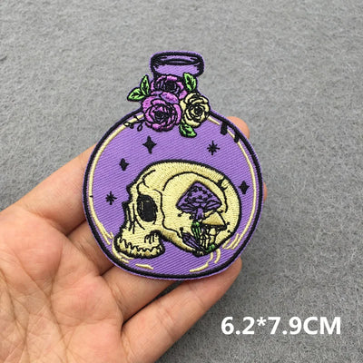 Skull and floral design patch held by a hand on a gray background