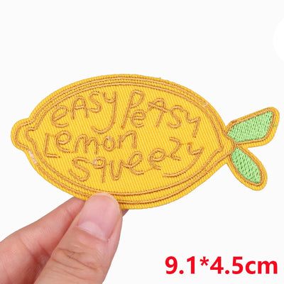 Yellow lemon-shaped patch with embroidered text held by a hand on a white background
