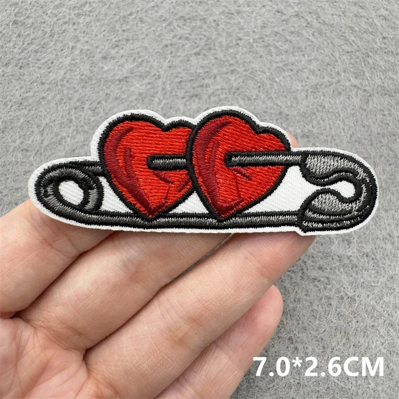 Embroidered patch with two red hearts and black text held by a hand on a gray background