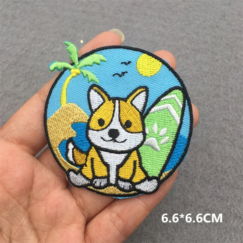 Embroidered patch of a corgi in a tropical setting held in a hand on a gray background.