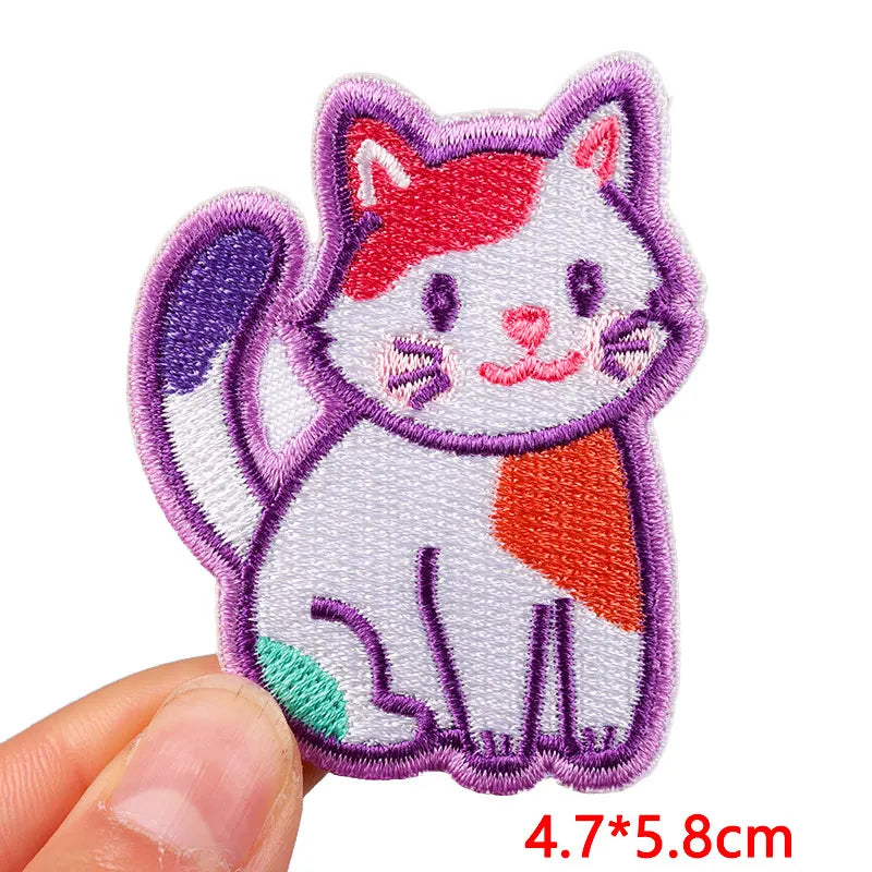 Embroidered patch of a cat with red and orange patches held by a hand on a white background.