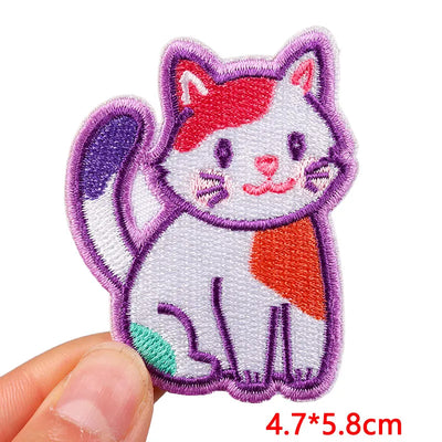 Embroidered patch of a cat with red and orange patches held by a hand on a white background.