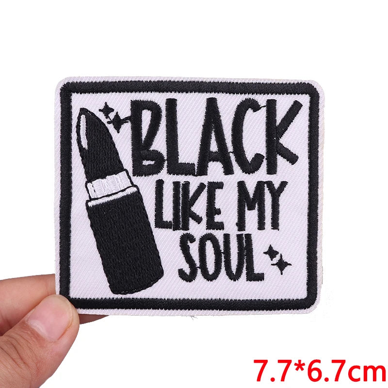 Embroidered patch with lipstick design and text 'Black Like My Soul' held by a hand.