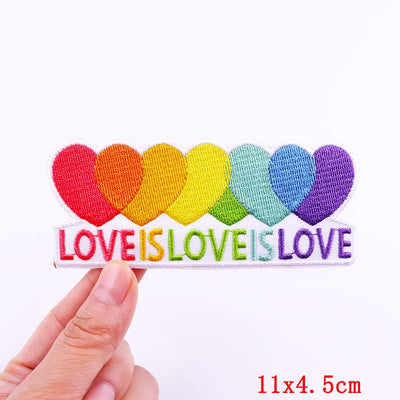 Rainbow heart patch with 'LOVE IS LOVE' text held by a hand on a white background