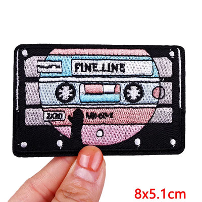 Cassette tape-shaped patch held by a hand with 'Fine Line' branding.
