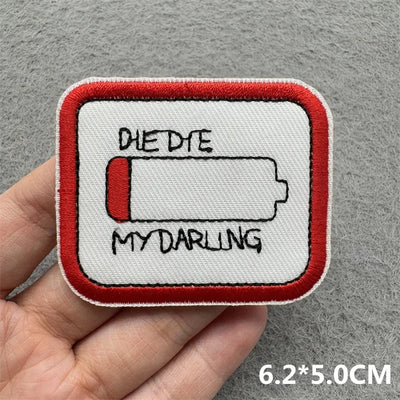 Patch with 'Dye Dye My Darling' text held in a hand on a gray background