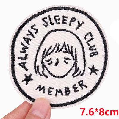 Circular patch with 'Always Sleepy Club Member' text and a face illustration, held by a hand.