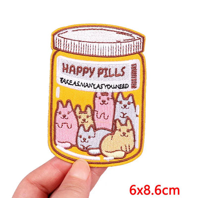 Embroidered patch of a jar labeled 'Happy Pills' with cartoon cats, held by a hand.