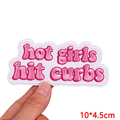 Embroidered patch with 'hot girls hit curbs' text held by a hand on a white background