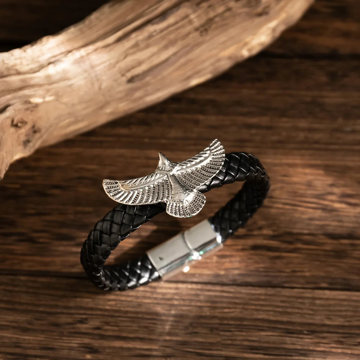 Black braided leather bracelet with silver eagle charm on a wooden surface