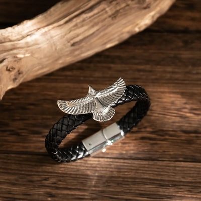 Black braided leather bracelet with silver eagle charm on a wooden surface