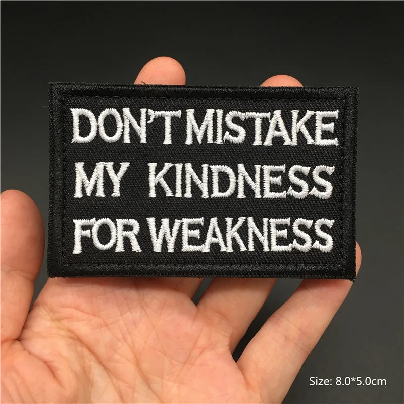 Hand holding a black and white Don’t Mistake My Kindness For Weakness embroidered hook-and-loop patch approx 8x5cm on a dark background