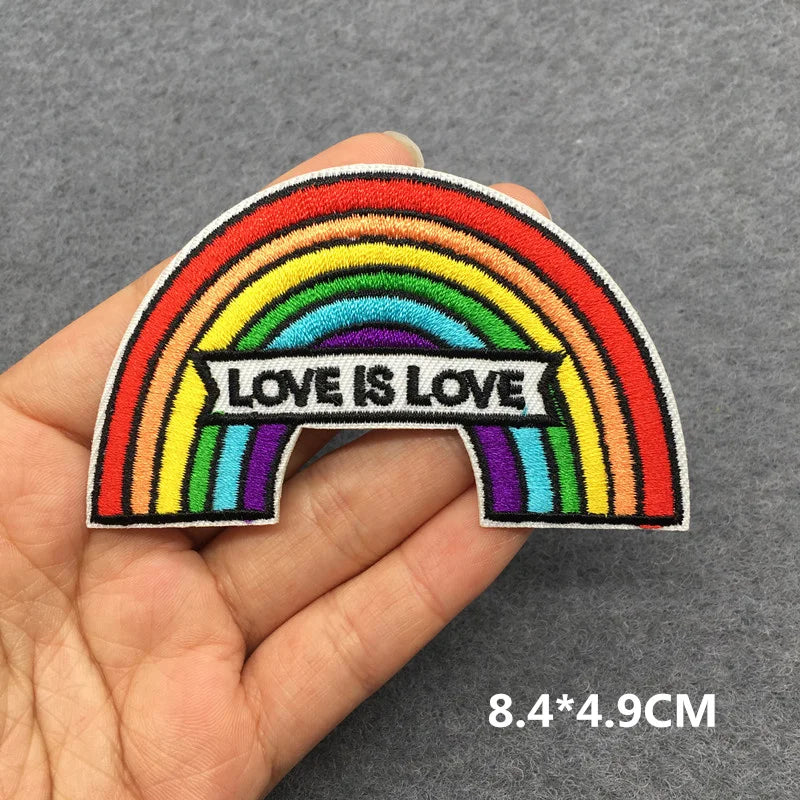 Rainbow patch with 'Love is Love' text held in a hand on a gray background