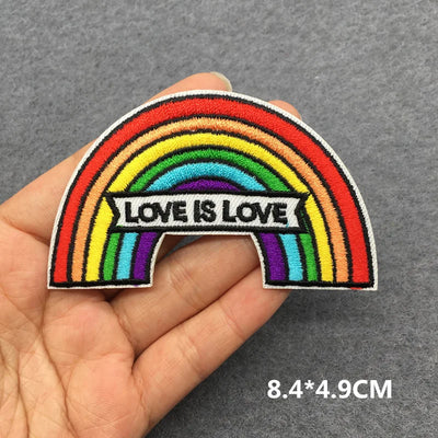 Rainbow patch with 'Love is Love' text held in a hand on a gray background