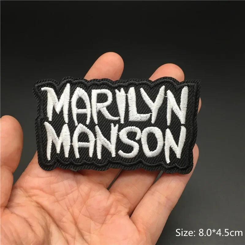 Hand holding a black and white Marilyn Manson embroidered iron-on patch 8x4.5cm on a dark background