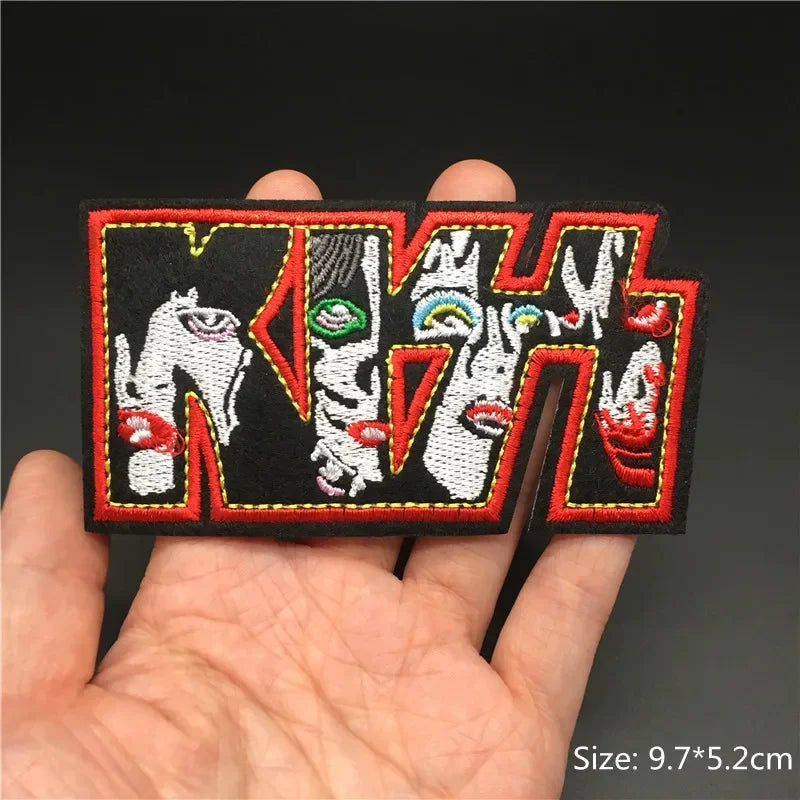 Hand holding a multicolor Kiss rock band embroidered iron-on patch 9.7x5.2cm on a dark background
