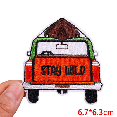 Embroidered patch of a van with 'Stay Wild' text held by a hand on a white background.