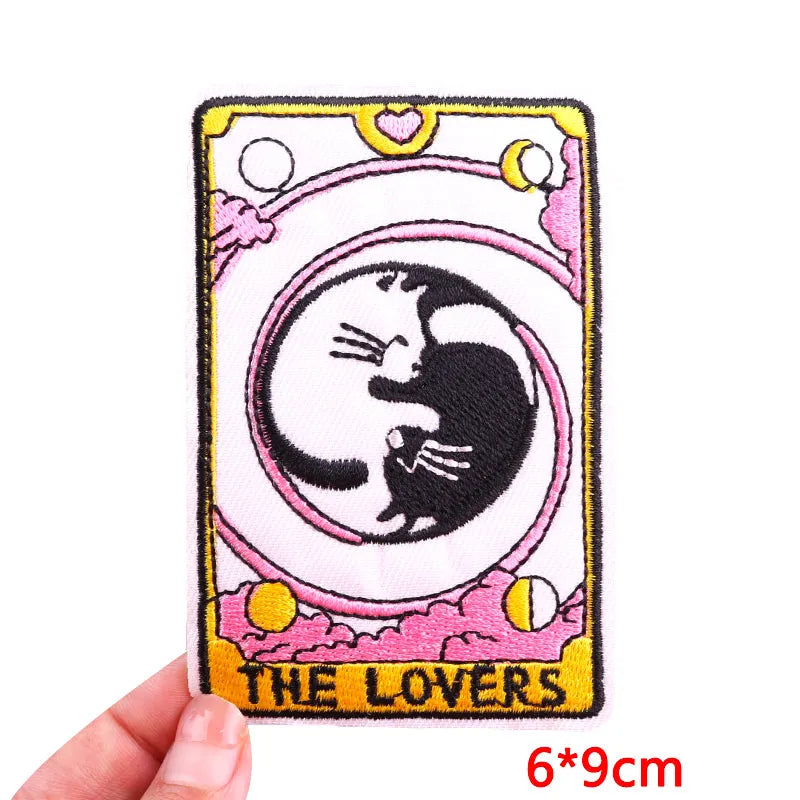 Embroidered patch of 'The Lovers' tarot card with cats, held by a hand.