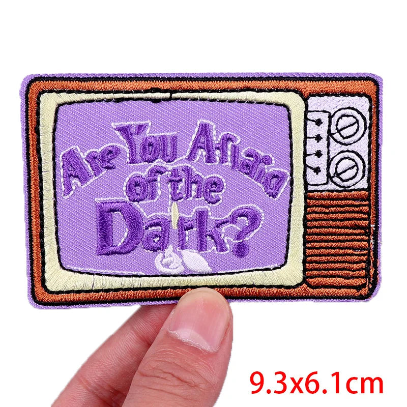 Embroidered patch with 'Are You Afraid of the Dark?' text on a television screen design, held by a hand.