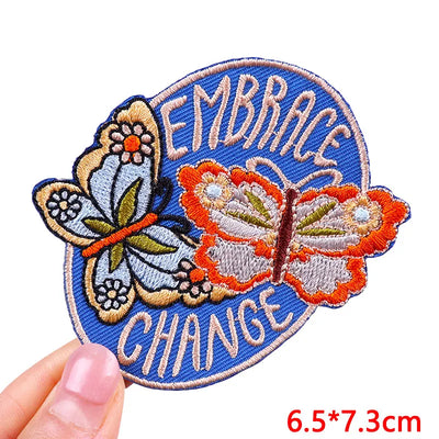 Embroidered patch with butterflies and 'Embrace Change' text held by a hand on a white background.