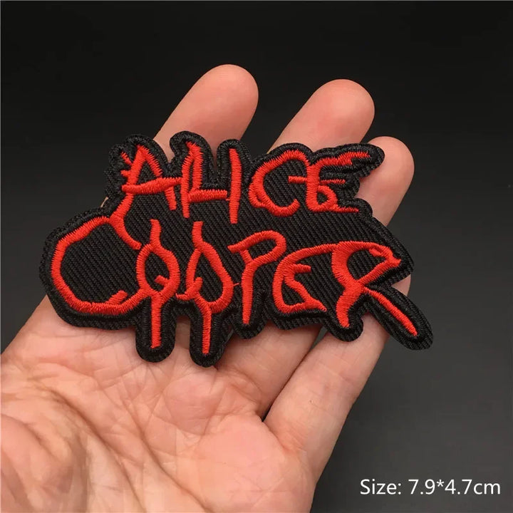 Hand holding a black and red Alice Cooper embroidered iron-on patch 7.9x4.7cm on a dark background