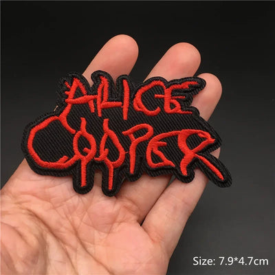 Embroidered patch with 'Alice Cooper' text held in a hand against a dark background