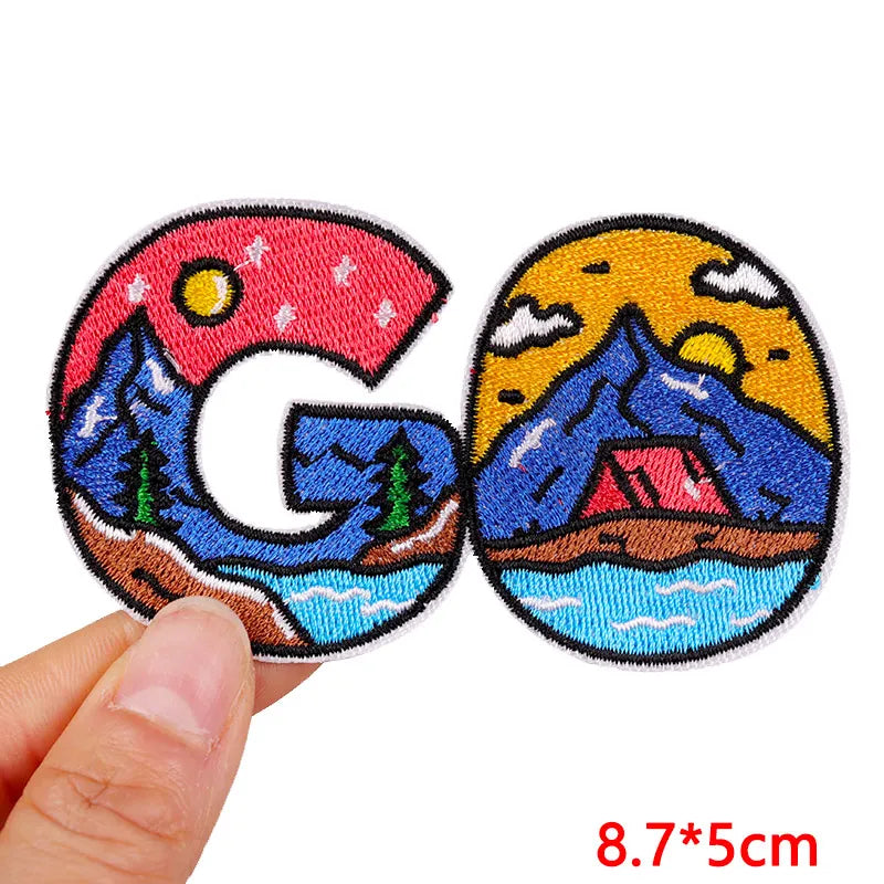 Two embroidered patches with mountain and camping design held by a hand, with size '8.7*5cm' displayed.