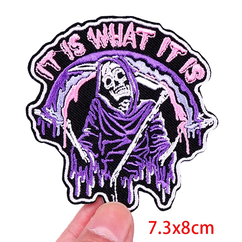 Patch with skeleton design and text 'IT IS WHAT IT IS' held by a hand, with dimensions 7.3x8cm.