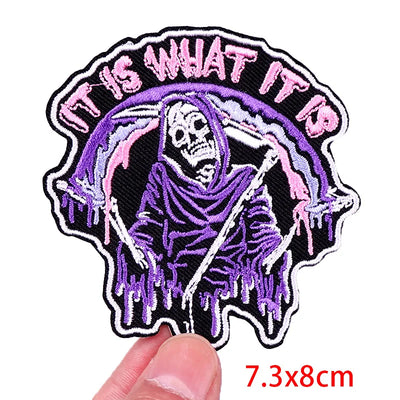 Patch with skeleton design and text 'IT IS WHAT IT IS' held by a hand, with dimensions 7.3x8cm.