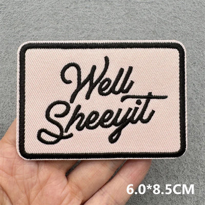 Patch with 'Well Sheeyit' text held by a hand against a gray background
