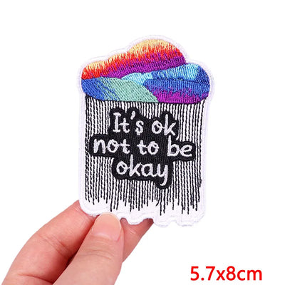 Patch with 'It's ok not to be okay' text held by a hand on a white background