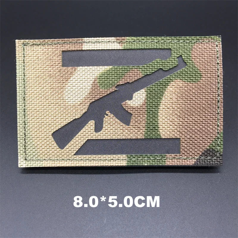 Hand holding a multicam rifle IR style hook-and-loop tactical badge approximately 8x5cm on a dark background