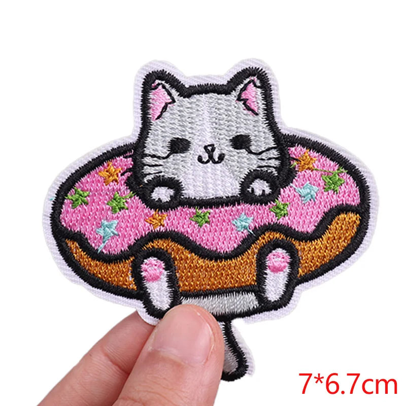 Embroidered patch of a cat on a donut held by a hand, with dimensions displayed.