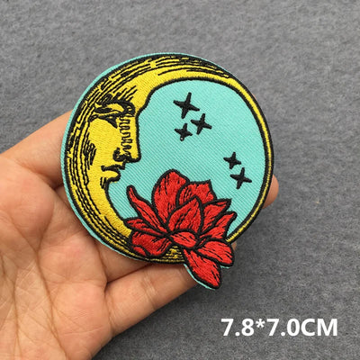 Embroidered patch with moon, stars, and red flower held in a hand on a gray background