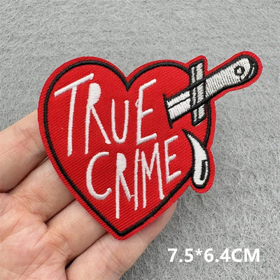 Heart-shaped patch with 'True Crime' text and a knife design held by a hand on a gray background.