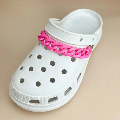 White clog shoe with a pink chain detail on a beige background