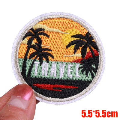 Embroidered patch with palm trees and 'Travel' text held by a hand on a white background.