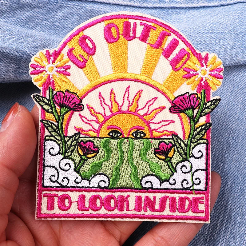 Embroidered patch with sun and flowers design held over a denim background