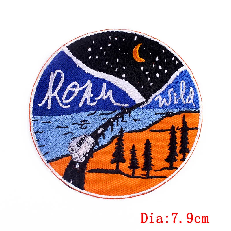 Round embroidered patch with a mountain scene, trees, and 'Roam Wild' text on a white background.