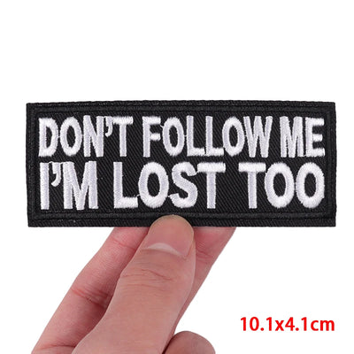 Black patch with white text 'DON'T FOLLOW ME I'M LOST TOO' held by a hand on a white background.